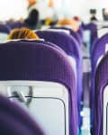 Airplane cabin with rows of purple seats and tray tables folded up.