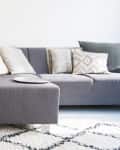 Gray sectional sofa with assorted pillows, small side table with decor, and a patterned rug on light wood floor.