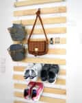 Wooden wall organizer with baskets, a brown bag, watch, keys, and three pairs of sneakers.
