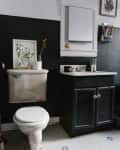 Bathroom with black walls, white toilet, black vanity, framed art, and hexagonal tile floor with blue accents.