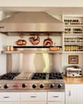 Stainless steel stove with copper cookware, spice rack, toaster, and wooden countertops in a cozy kitchen.