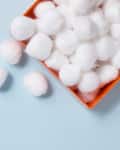 Cotton balls in an orange box on a light blue surface.