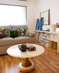 Living room with beige sofa, colorful patterned cushions, round marble coffee table, and shelves with storage boxes.