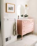 A pink dresser-turned-sink in a warm white bathroom with wainscoting
