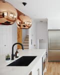 Modern kitchen with white cabinets, stainless steel fridge, copper pendant lights, and black sink faucet.