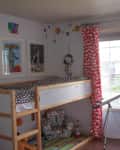 Child's room with a wooden loft bed, space-themed decor, red curtains, and a telescope by a large window.