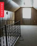 Attic room with wood paneling, carpeted floor, and a single window. Black metal railing on the left side.