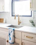 White kitchen with gold faucet, blue-trimmed window, and blue tie-dye towel on sink.