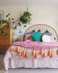 Bohemian bedroom with rattan headboard, pink bedding, orange tassels, and lush hanging plants.