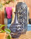 Blue decorative vases on a wooden table with a potted plant, wicker chair, and pink throw in the background.