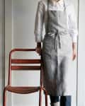 Person in a striped apron and white shirt standing beside a red metal chair.