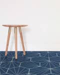 Wooden stool on geometric-patterned navy floor against a white wall.