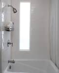 White tiled bathroom with a bathtub, showerhead, and a window. Wall-mounted caddy holds toiletries.