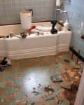 Bathroom renovation in progress with tools on the tub, blue tile walls, and a partially removed checkered floor.