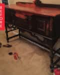 Antique wooden sideboard with ornate carvings, red paint, sandals, a paint can, and a glass on the floor.