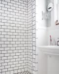 Shower with white subway tiles and black grout, hexagonal floor tiles, and a wall-mounted sink.