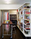 Modern kitchen with white cabinets, dark wood floor, rolling island, bar stools, and a large bookshelf filled with books.