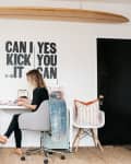 Woman working at a desk in a home office with a surfboard on the wall and motivational text art.