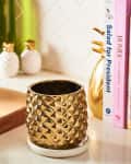 Pineapple on a cutting board with a knife, next to a gold pineapple-shaped mug and cookbooks.