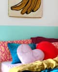 Colorful bedroom with heart-shaped pillows, banana wall art, and headphones hanging on a slatted headboard.