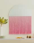 Pink fringe wall art above a console table with vases, plants, and small decor items.