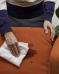 A man presses the stain of an orange upholstery fabric dry with a cloth