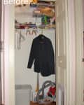 Small closet with vacuum, storage bins, hanging jacket, and cluttered shelves.