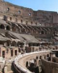 Interior view of the Colosseum in Rome, showcasing ancient stone arches and tiered seating under a clear sky.