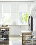 Modern kitchen with white cabinets, stainless steel appliances, wooden island, and dining table under a decorative pendant light.