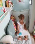 Child reading a book in a cozy nook with colorful pillows and wall shelves filled with books.
