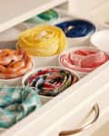 Drawer with neatly rolled colorful scarves in individual compartments.
