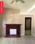 Empty room with red brick fireplace, beige walls, tiled floor, and ceiling fan.