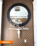 Round mirror with black frame above a white shelf on patterned brown wall, decorative branches on shelf.