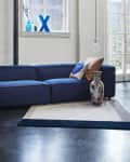 Blue sectional sofa with colorful cushions, geometric ottoman, and decorative vase in a modern living room.