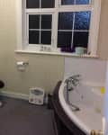 Bathroom with patterned wallpaper, white sink, toilet with dark seat, corner bathtub, and frosted window.