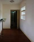 Narrow hallway with wooden floor, glass shelf, and view into a small kitchen with tiled walls.