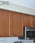 Wooden kitchen cabinets with a stainless steel microwave below, set against floral wallpaper.