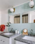 Double vanity bathroom with granite countertops, blue tile backsplash, round mirrors, and red towels.