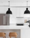 Modern kitchen with white cabinets, black pendant lights, stainless steel fridge, and wooden bar stools at the island.