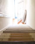 Carpeted staircase with a rolled-up rug at the bottom near a bright doorway.