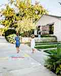 Two children walking on a sidewalk towards a modern house with a red mailbox and large house numbers 15 and 19.