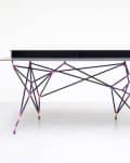 Modern desk with a geometric metal frame in multicolored hues and a sleek black tabletop.