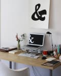 Home office desk with laptop, keyboard, books, red mug, lamp, and ampersand poster on wall.