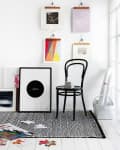 Black chair on patterned rug, surrounded by framed art, colorful prints, and puzzle pieces on a white floor.