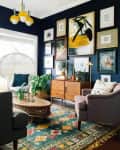 Eclectic living room with dark walls, colorful rug, mid-century sideboard, gallery wall, and modern yellow chandelier.
