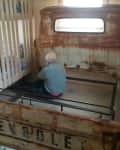 Man assembling a bed frame made from rusted Chevrolet truck parts in a wooden room.