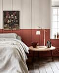 Bedroom with striped bedding, wooden side table, lamp, and floral painting on a two-tone wall.