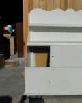 White wooden shelf unit with two shelves and a scalloped top, set against a wooden background.