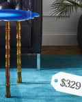 Blue side table with gold bamboo legs on a teal rug, next to a dark sofa, priced at $329.