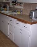 Kitchen counter with white cabinets, a silver toaster, dish rack, and potted plants on the windowsill.
